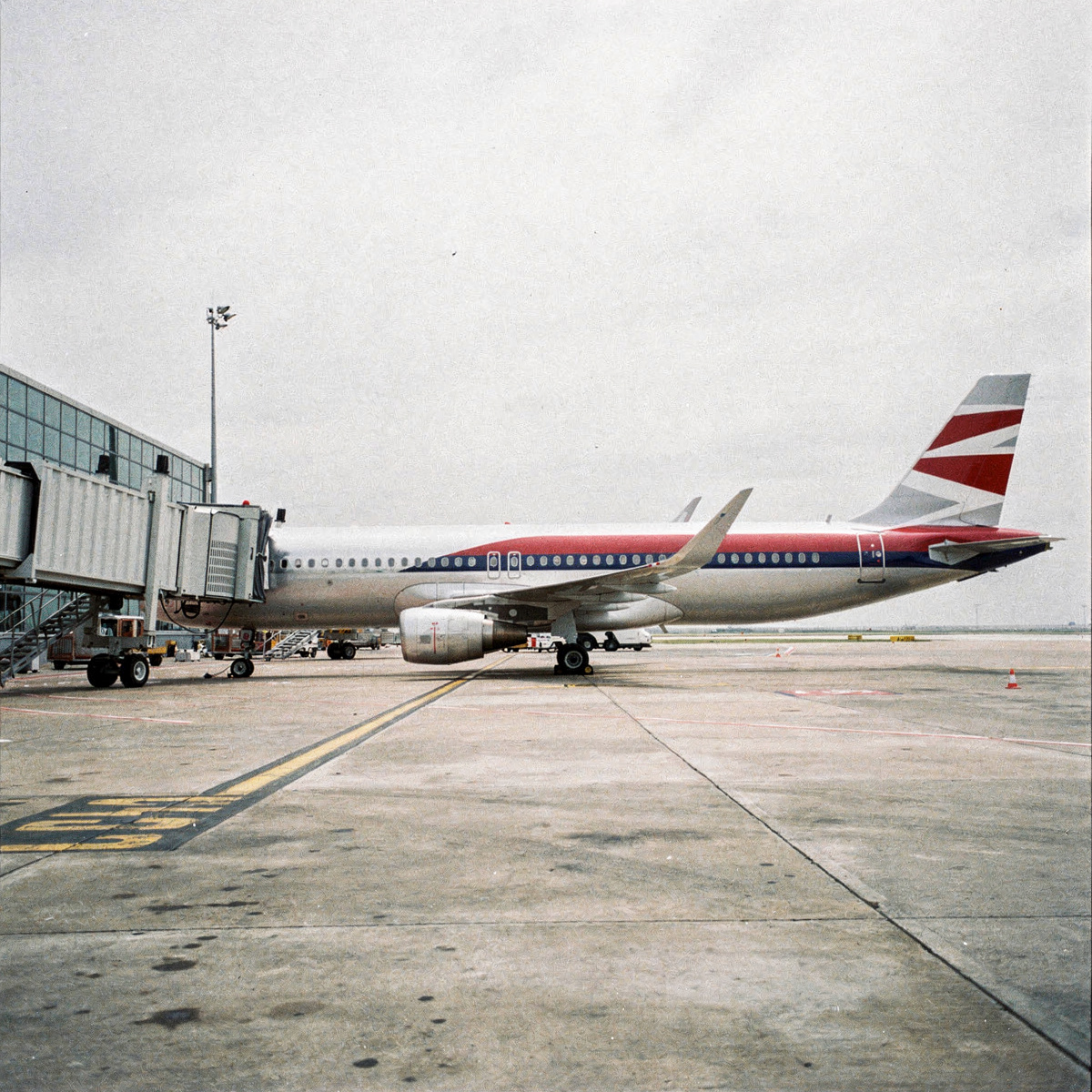 A single A320 family aircraft is parked at a gate on a bright, overcast day, with a jetbridge connected to its forward door.