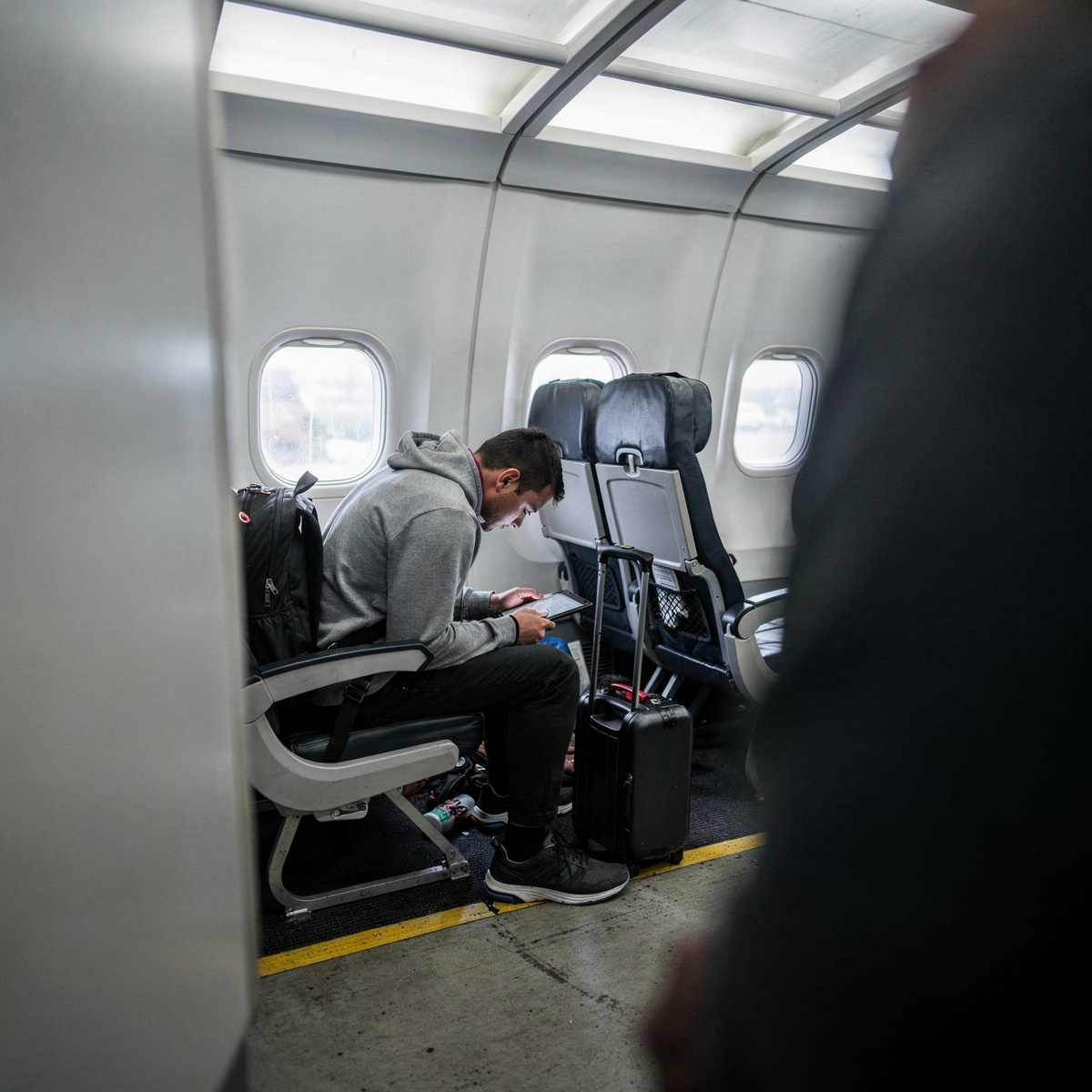 A passenger in a generic airline cabin, focused on a tablet, with the cabin environment suggesting routine travel.