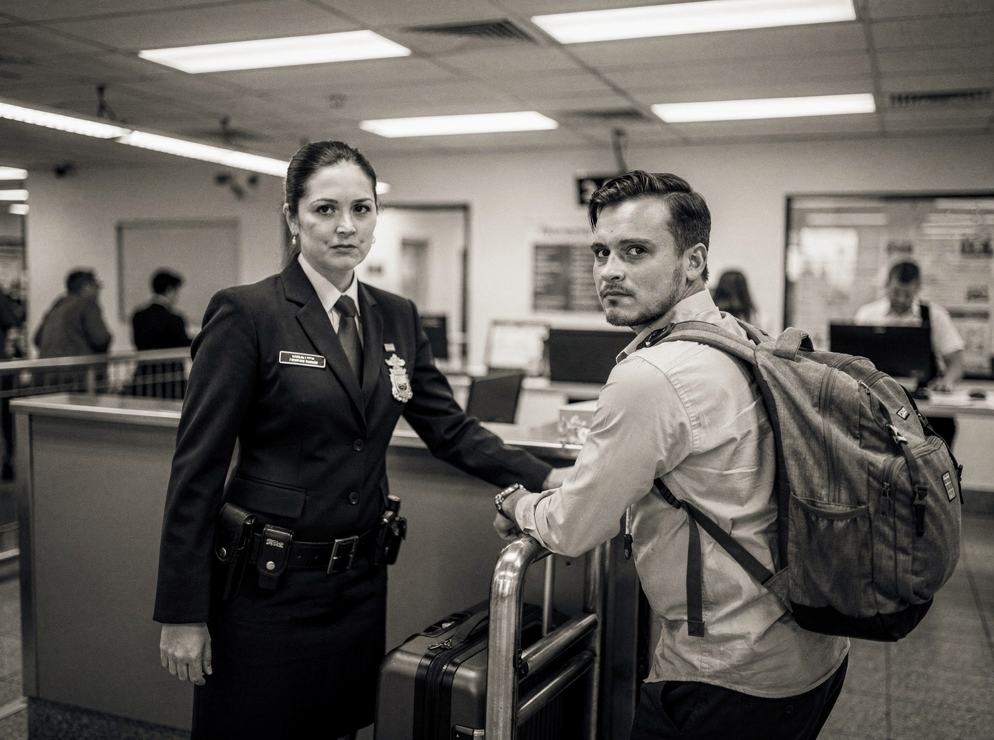 An Australian border control officer stands at a customs checkpoint, examining a passenger's luggage. It is daytime.
