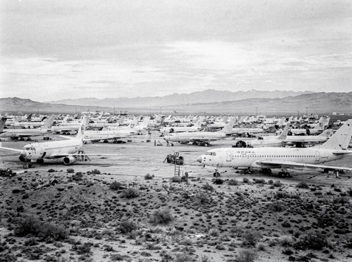 A wide shot of an aircraft boneyard under an overcast sky, with rows of decommissioned aircraft stretching into the distance.