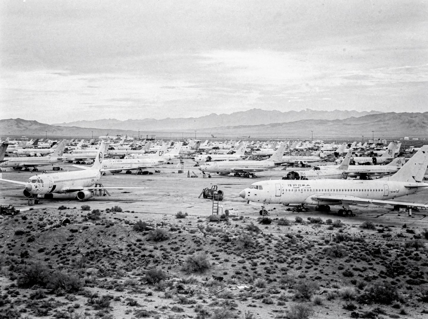 A wide shot of an aircraft boneyard under an overcast sky, with rows of decommissioned aircraft stretching into the distance.