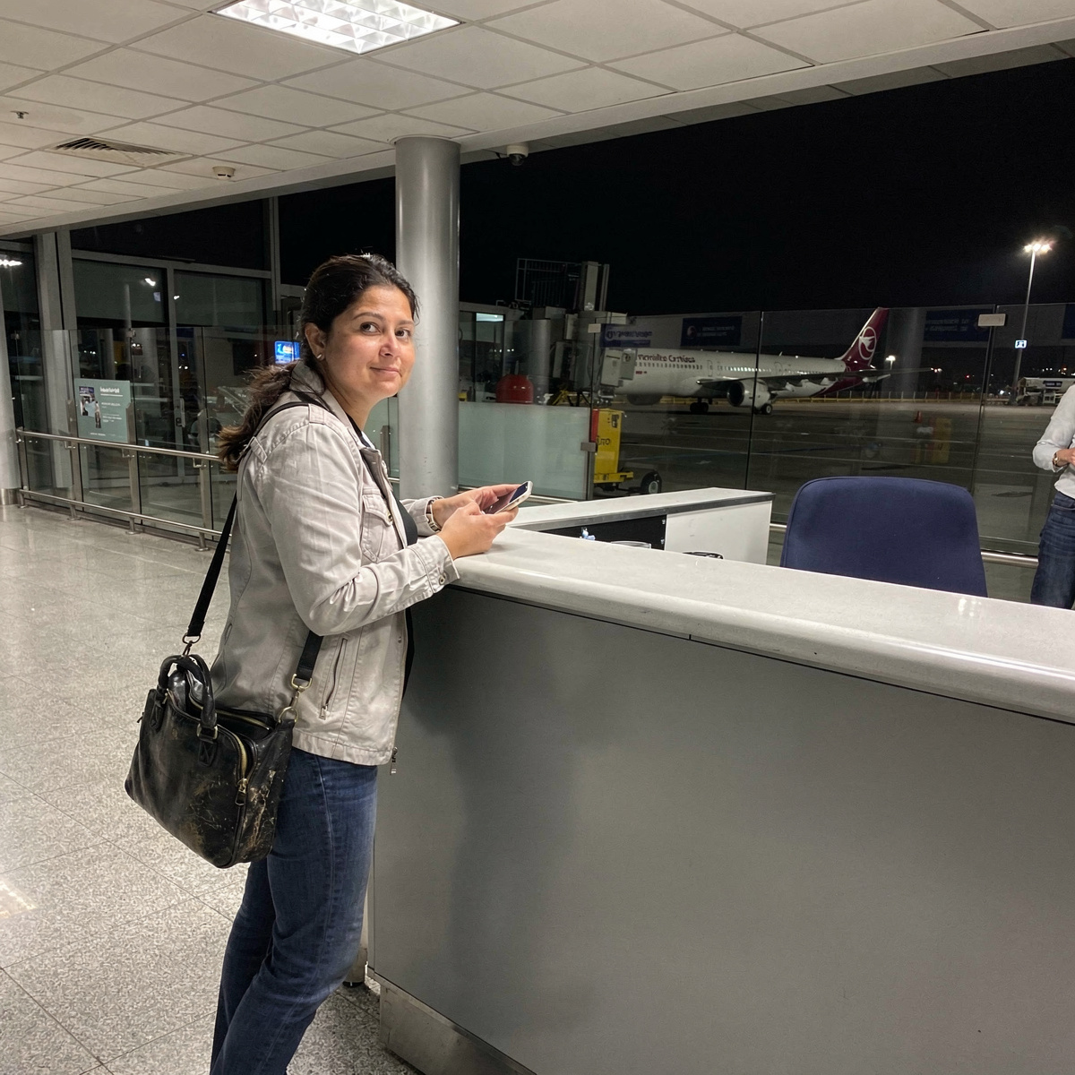 An airport gate area at night, after a flight cancellation, with a passenger making alternative arrangements.