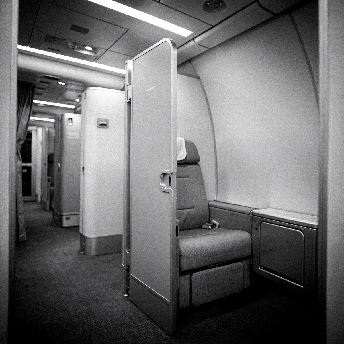 An empty first suite on an Airbus A380, with its door slightly ajar, under standard cool white overhead cabin lighting.