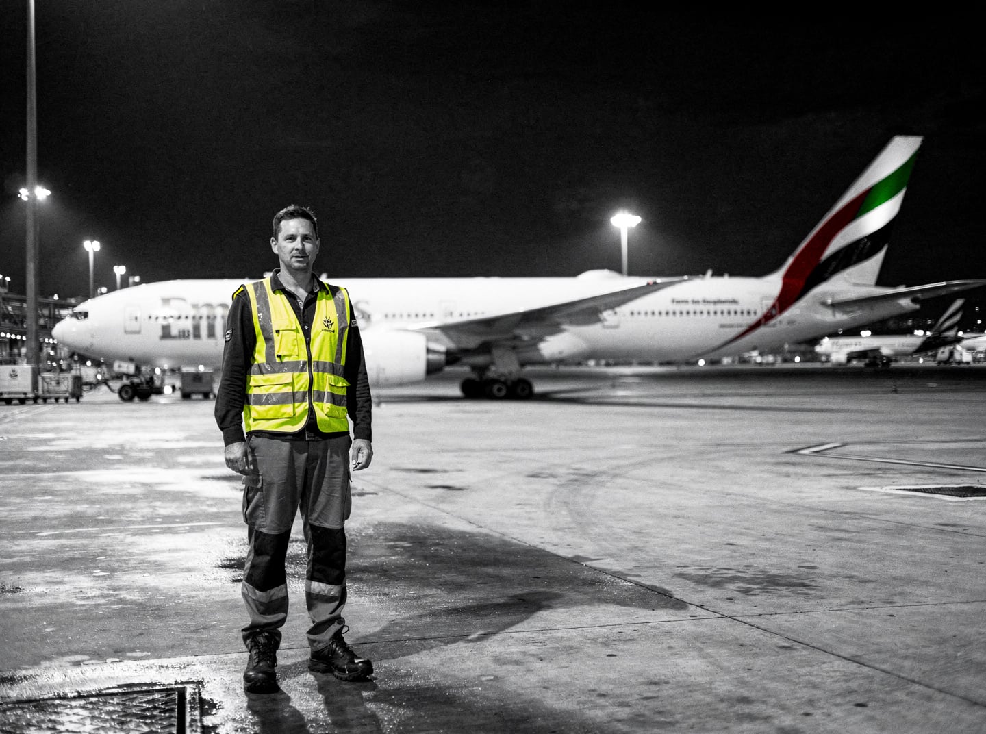 Sydney Airport's apron at night, with an Emirates Boeing 777-300ER parked under floodlights, suggesting a late-night operation during a curfew period.