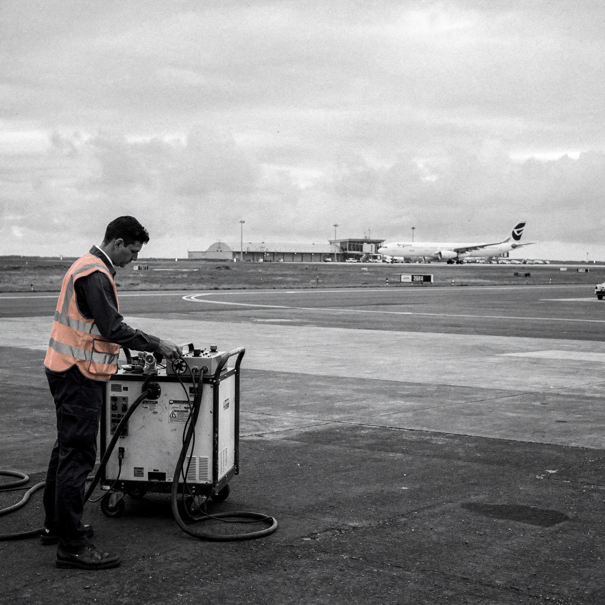 An Airbus A330-300 parked on a remote apron at a small island airfield under overcast skies, with ground crew working around it.