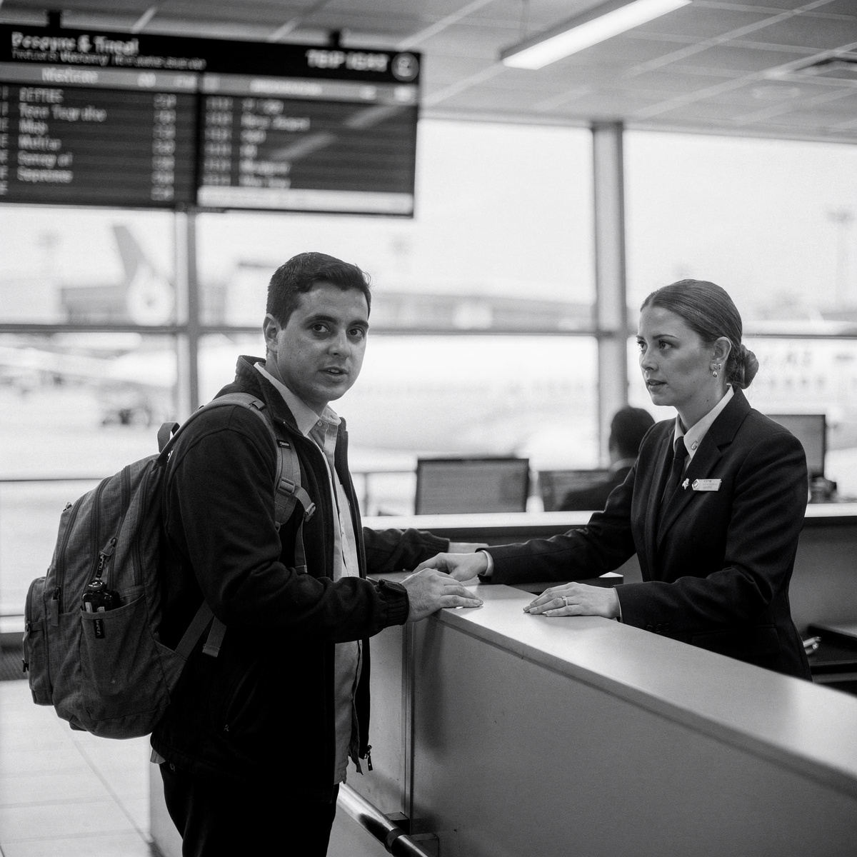 Midday at a busy airport gate, a passenger stands at the counter with a gate agent.