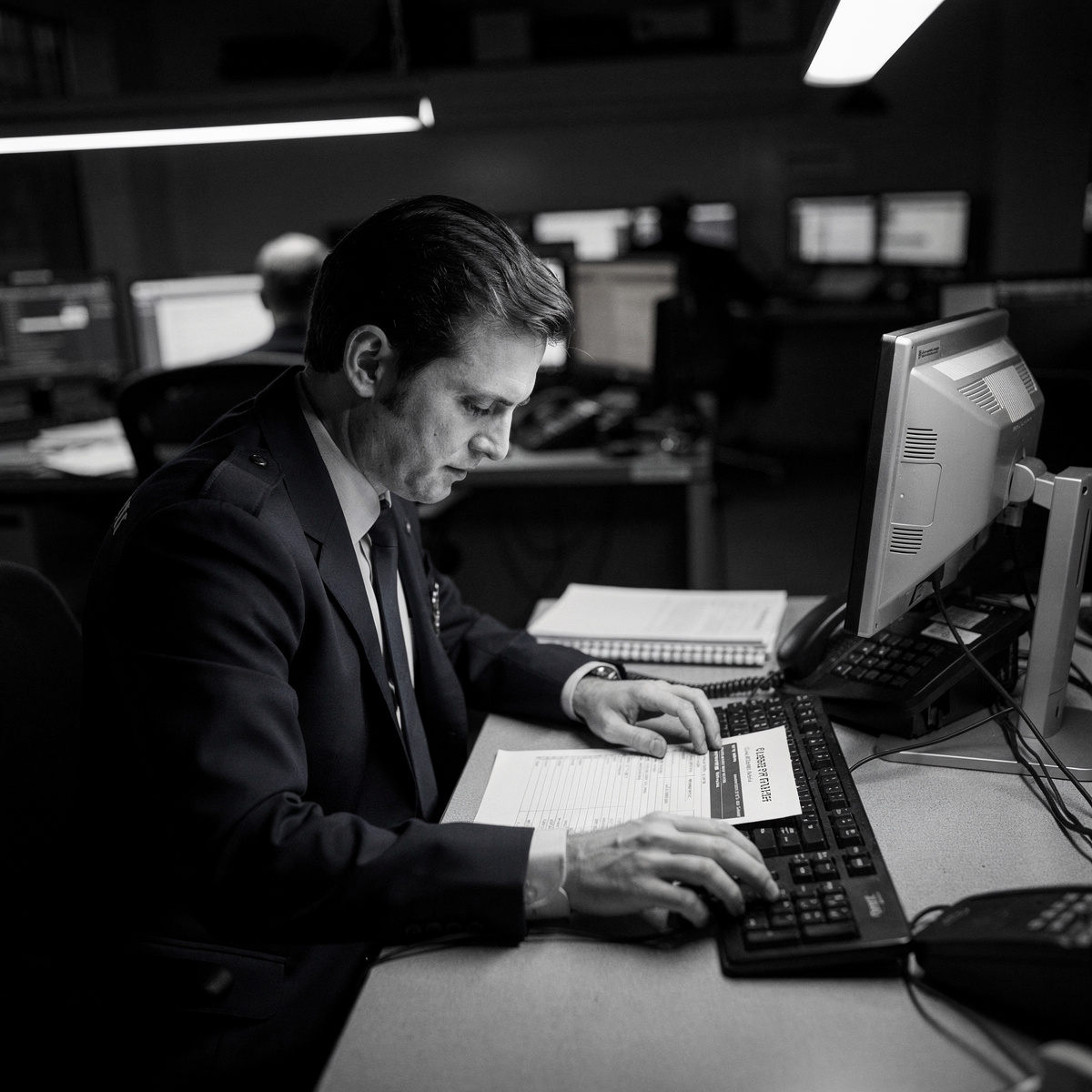 A dispatcher's desk in a dimly lit operations center, late at night, with a single figure focused on a document.
