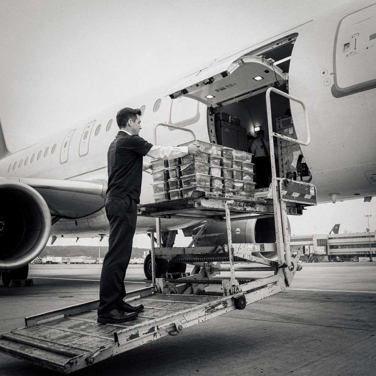 A refrigerated high-loader truck positioned at the side of a wide-body aircraft, its lift platform raised to the galley door.