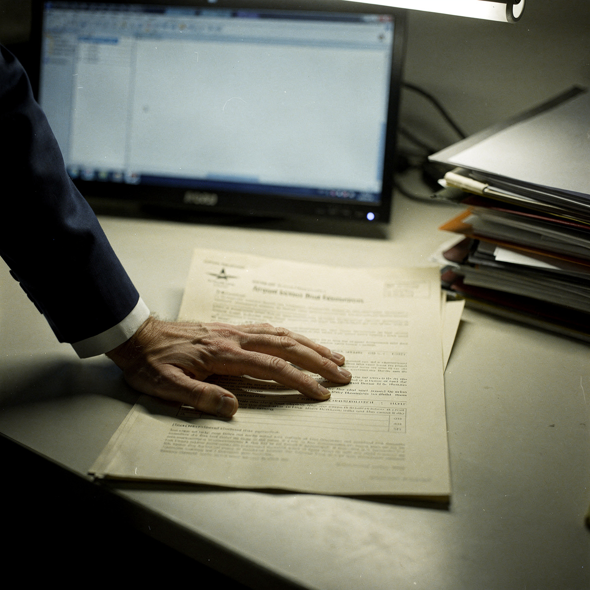 A document detailing airport slot regulations lies on a plain desk, illuminated by the cool glow of a monitor, with a hand poised to interact with it.