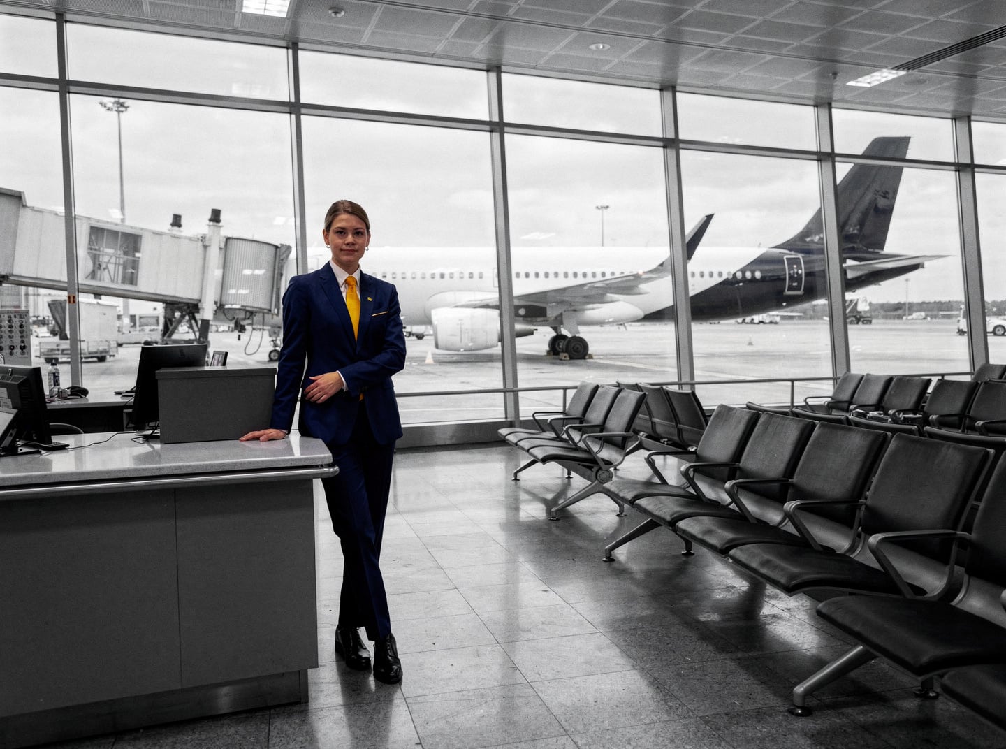 An empty departure gate at a major European hub airport during the day, with an Airbus A320 family aircraft visible through the glass.