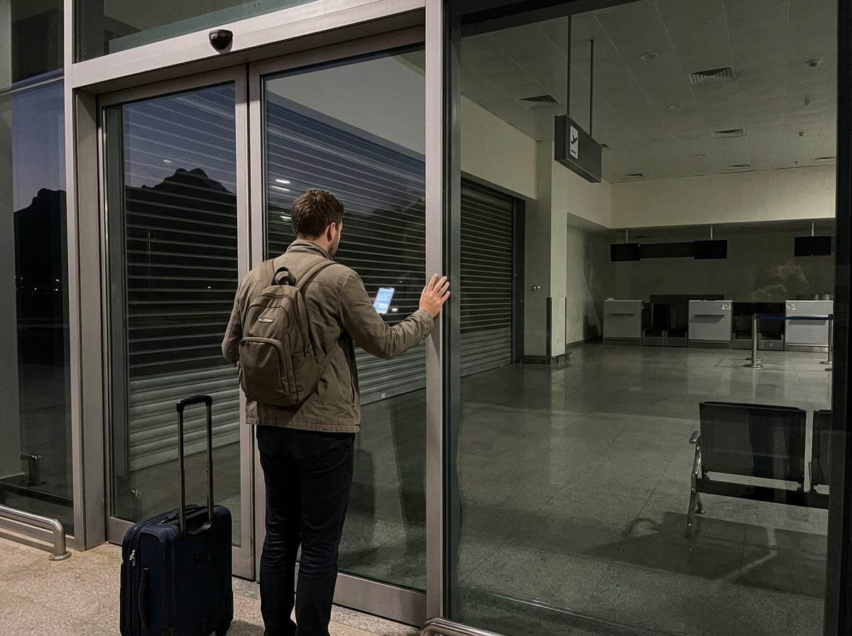 Traveler at closed southern Saudi airport terminal doors at night (ATC Intel)