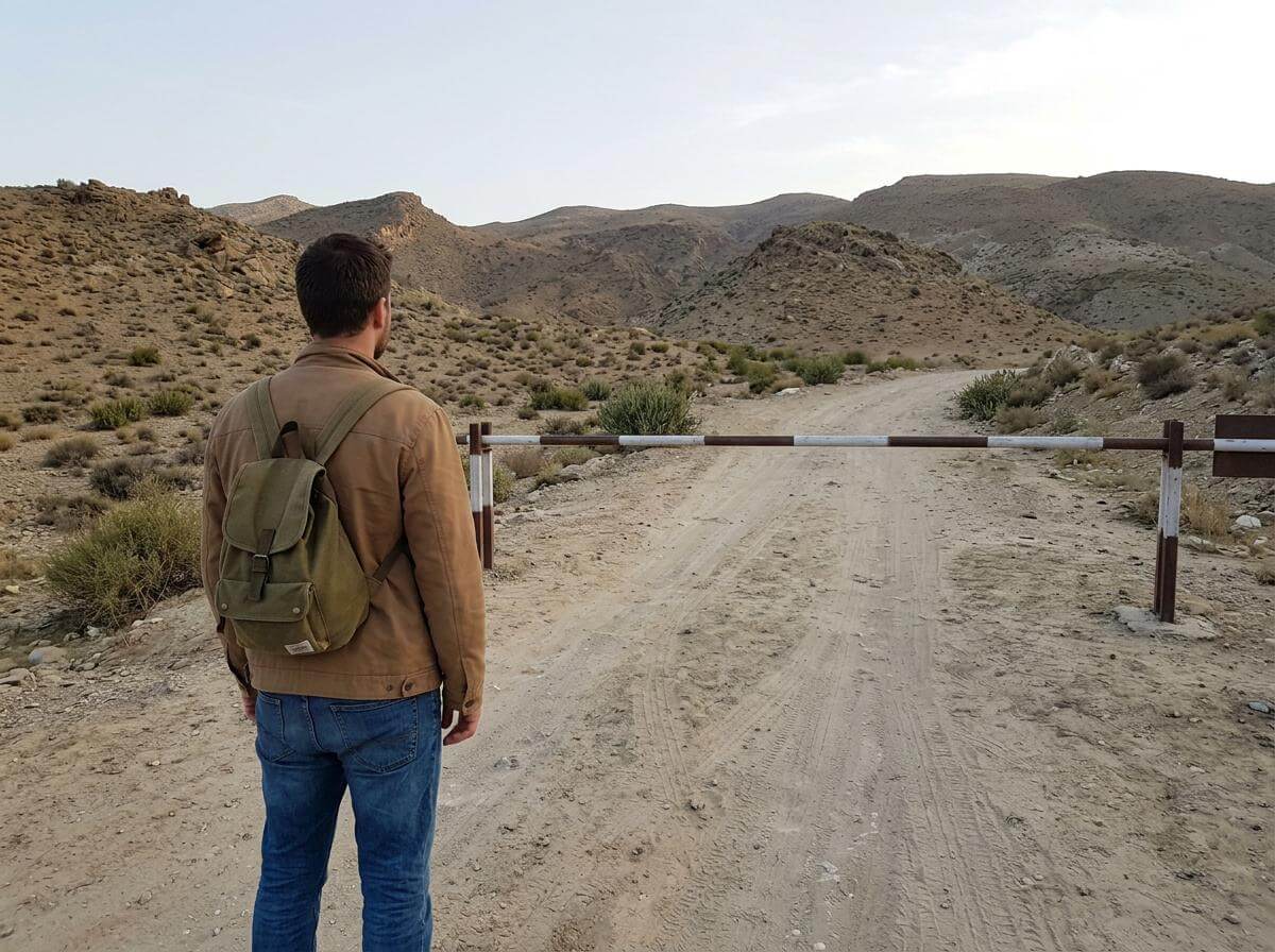 Traveler with a backpack facing a closed barrier on a dusty Pakistan border road (ATC Intel)