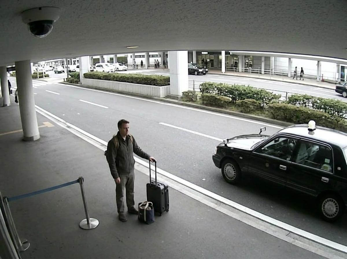 Traveler with suitcase waiting at a taxi rank outside a Tokyo airport terminal (ATC Intel)