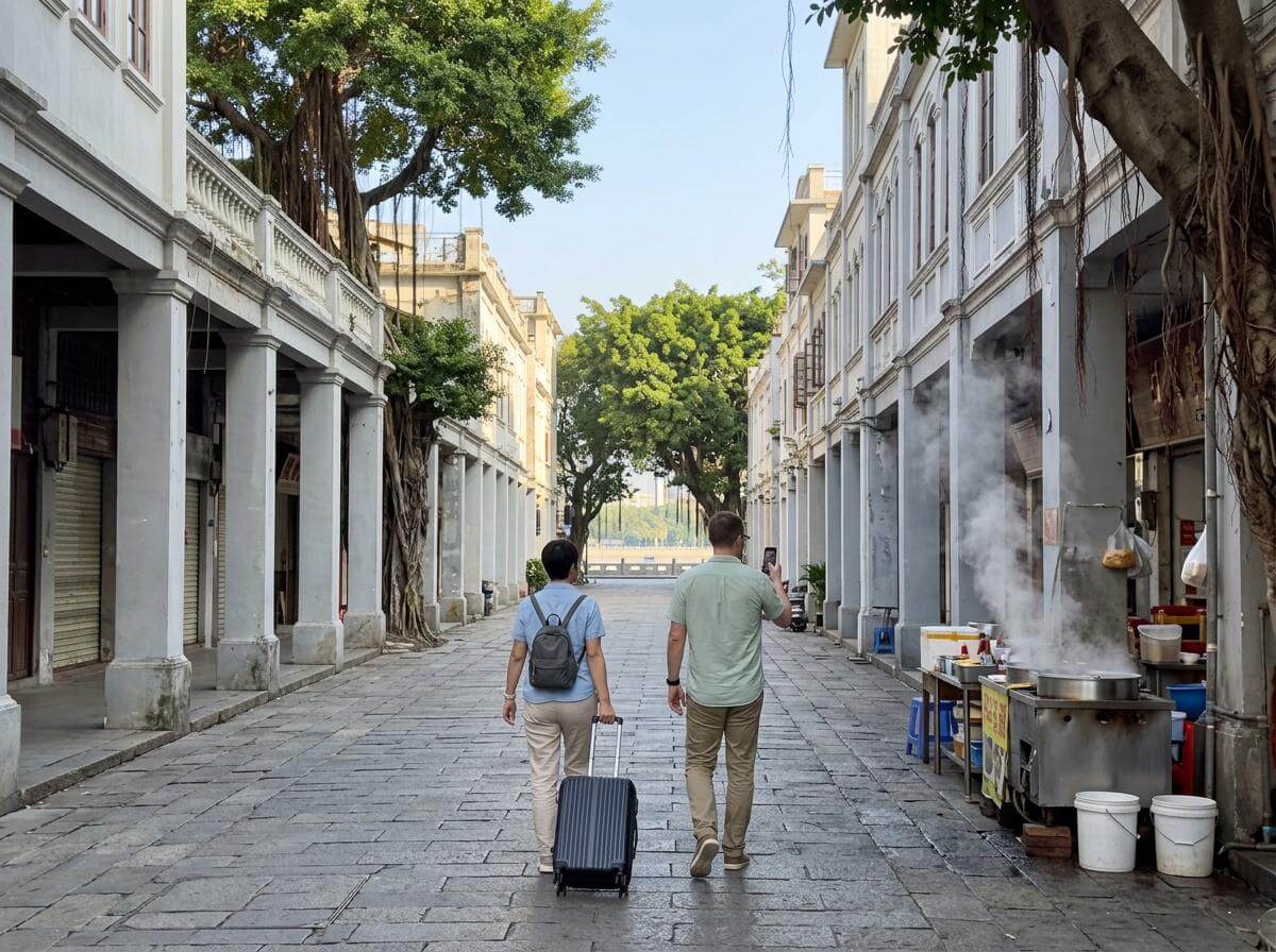 Travelers walking a Guangzhou street with arcade shophouses and banyan trees (ATC Intel)