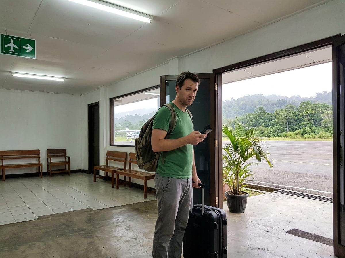 Traveler with backpack at a small Papua airport terminal checking his phone (ATC Intel)